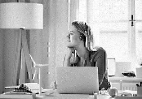 Frau mit Kopfhörern sitzt an einem Schreibtisch mit Laptop